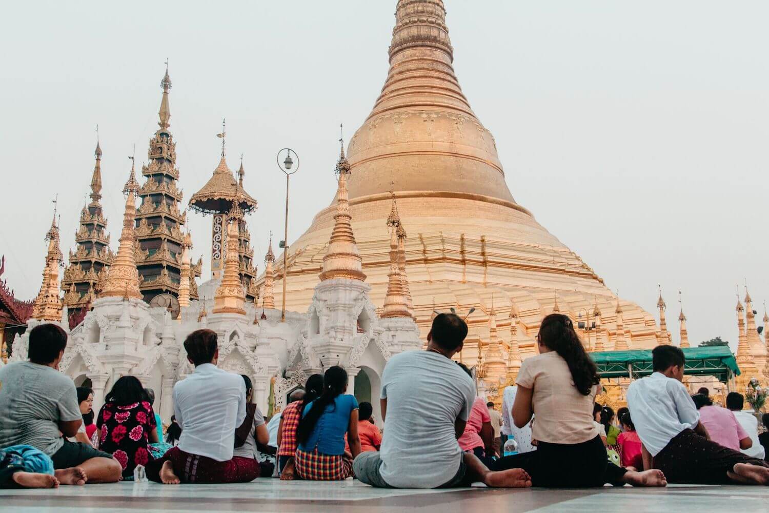 Best Myanmar Itinerary: Photo of Shwedagon Pagoda in Yangon Myanmar, the Golden Temple, with people sitting beneath the tallest spire at dusk. photo taken by Ryan Brown of Lost Boy Memoirs with Canon 650D Rebel T4i, edited in Lightroom.