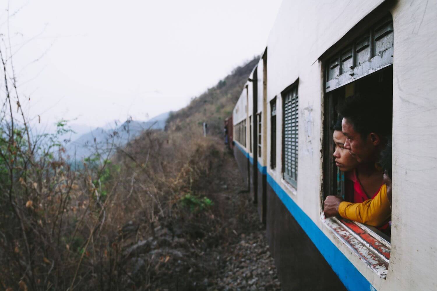 Best Myanmar Itinerary: Photo of two Myanmar people looking out of the old train window from Mandalay to Hsipaw down into the valley from the Goteik Viaduct. Photo by Ryan Brown of Lost Boy Memoirs, edited in Lightroom.