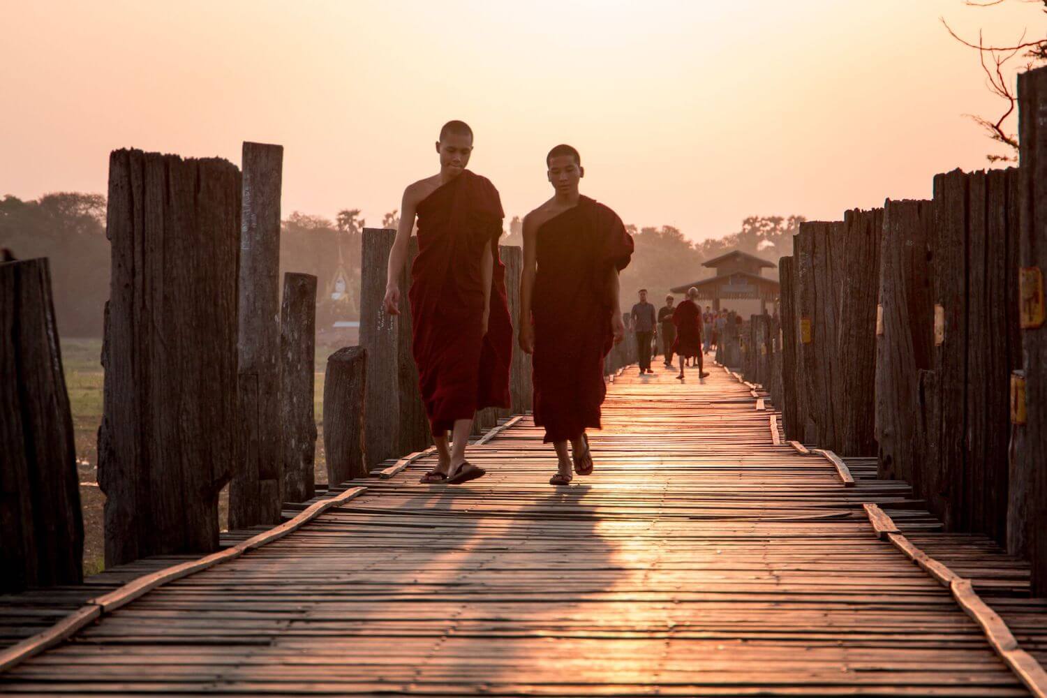 Best Myanmar Itinerary: Photo of two monks in crimson robes walking along U Bein Bridge in Mandalay Myanmar at sunrise. Photo taken by Ryan Brown of Lost Boy Memoirs, edited in Lightroom.