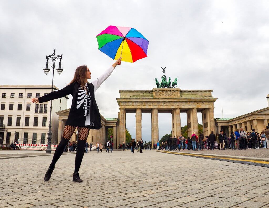 A woman standing in front of a historic monument in Berlin holding a colorful umbrella to the sky