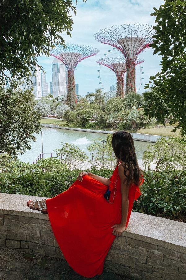 Woman sitting on a concrete wall in a red dress overlooking the Singapore supertree grove at Gardens by the Bay.