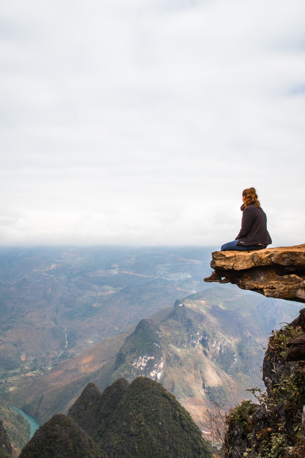 A solo woman overlooking the landscape in Vietnam while sitting on a rock.